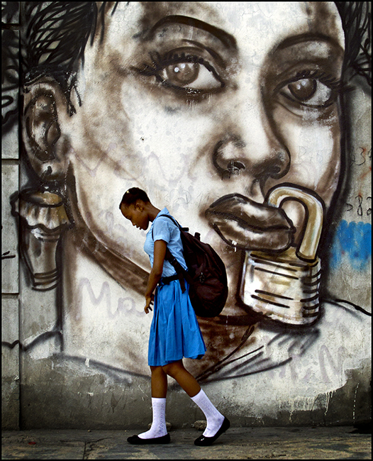 A student of a girls’ school in Port-au-Prince walks by a mural depicting the suppression of women in Haiti. Photo by Patrick Farrell